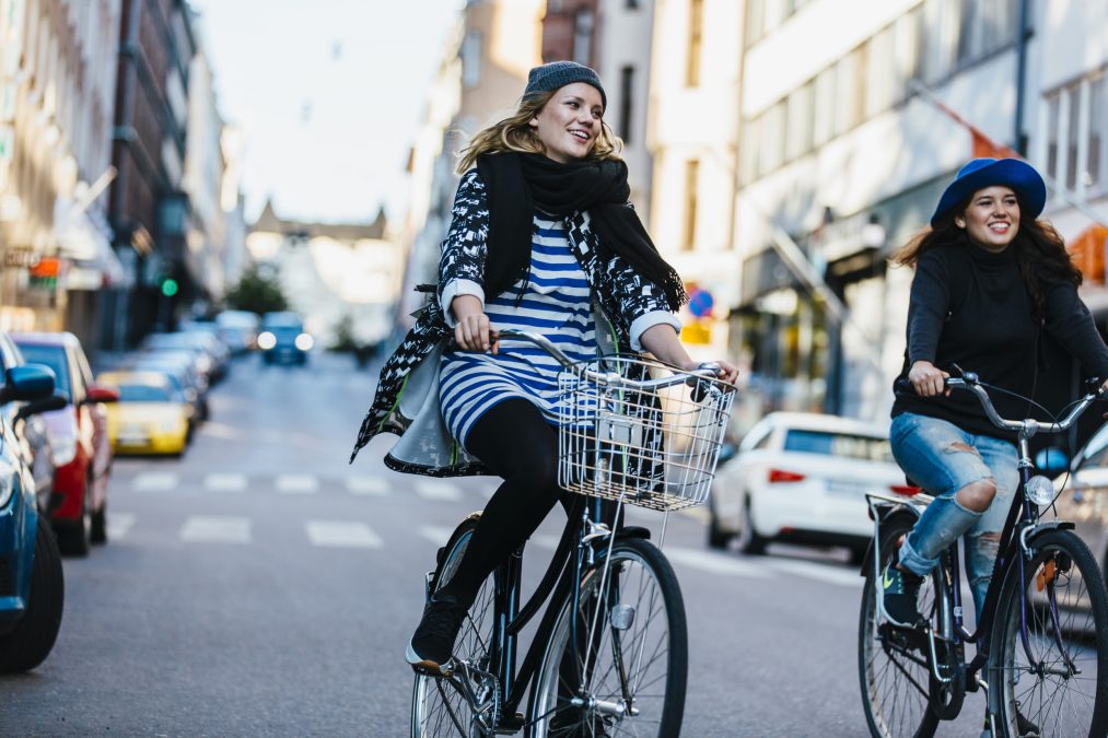 Kaksi pyöräilijää pyöräilevät iloisesti kadulla.